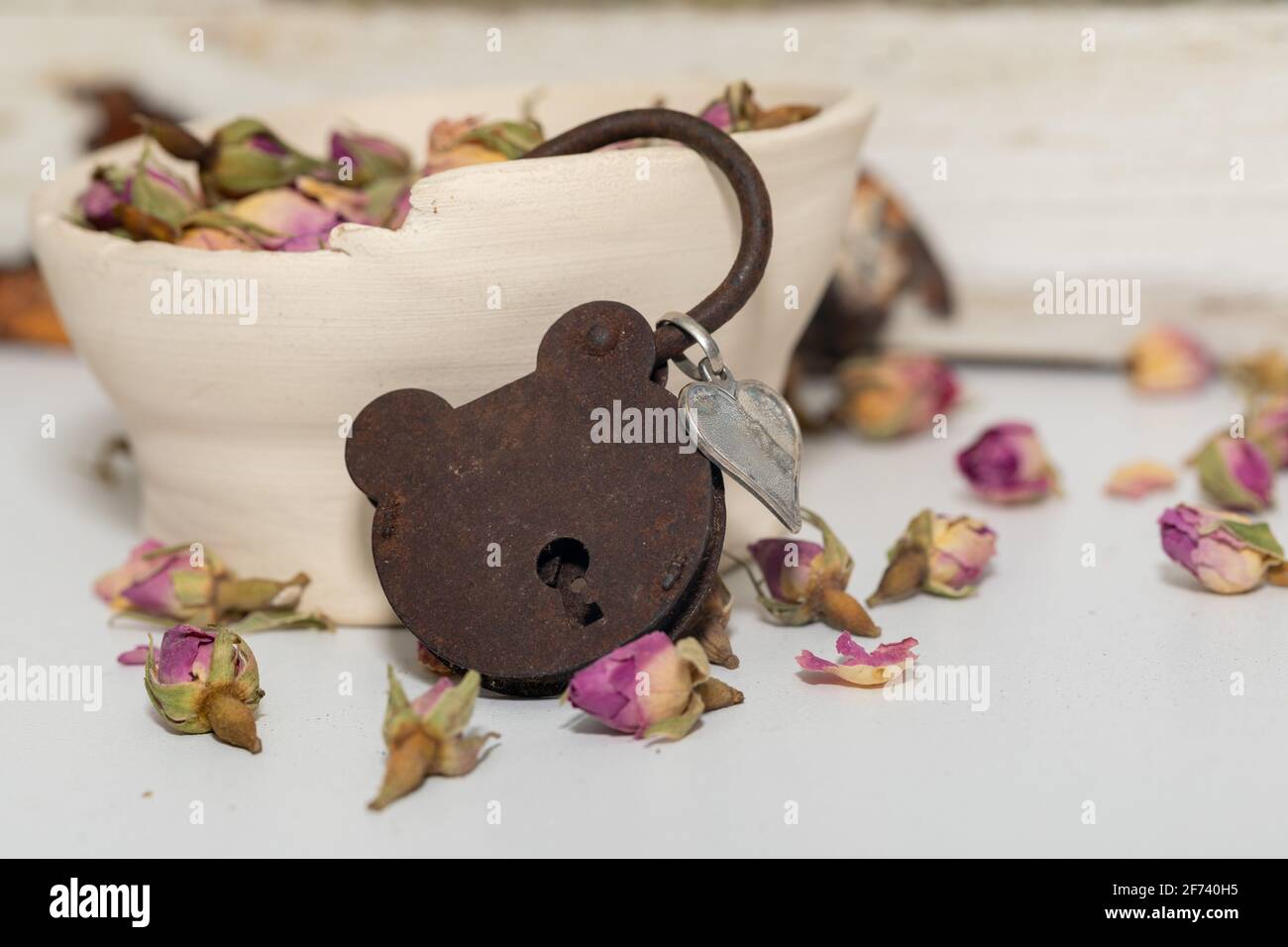 arrugginito vecchio lucchetto vintage che assomiglia a un orsacchiotto viso, ancora vicino alla finestra con una ciotola di rose secche Foto Stock