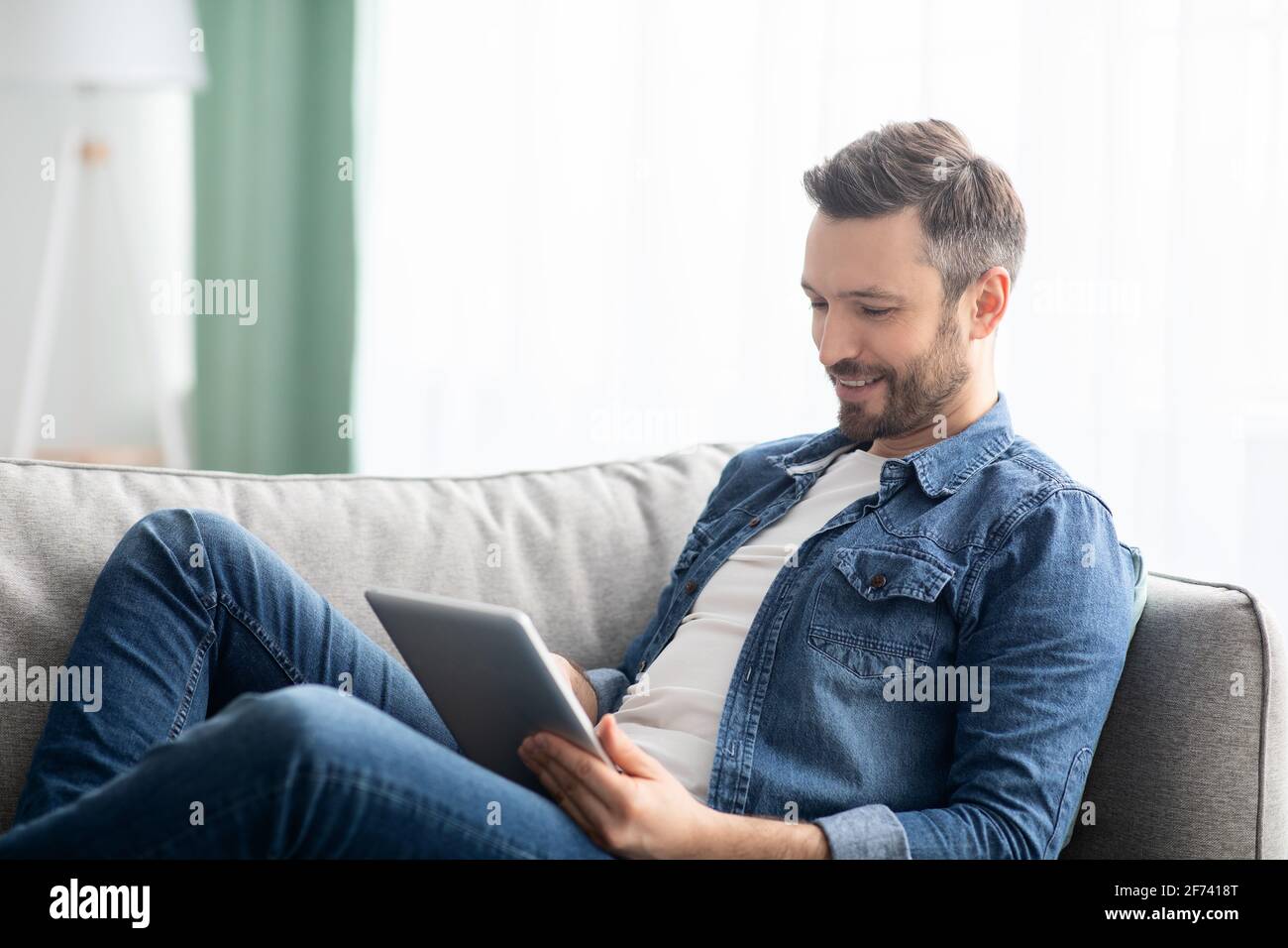 Uomo felice che si distende sul divano a casa, utilizzando un tablet digitale Foto Stock