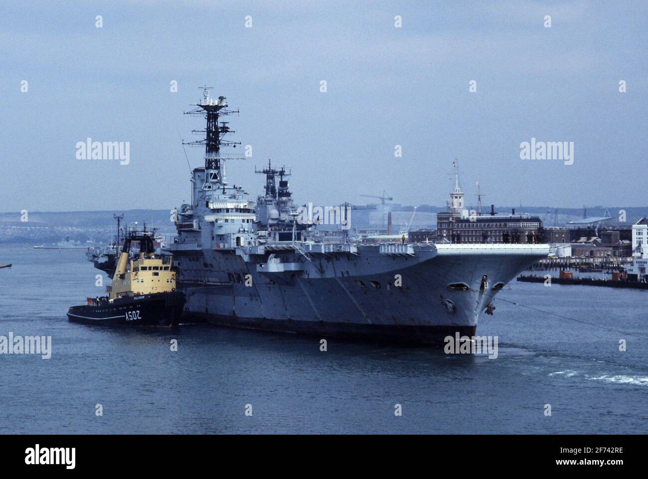 AJAXNETPHOTO. 10 APRILE 1984. PORTSMOUTH, INGHILTERRA. - SCRAPYARD BOUND - LA PORTAEREI HMS BULWARK, 'ARRUGGINITA B', CHE È STATO TRAINATO FUORI DALLA BASE NAVALE AL DEPOSITO DI ROTTAMI A CAIRNRYAN 1984. FOTO:JONATHAN EASTLAND/AJAX. REF:841843 64 Foto Stock