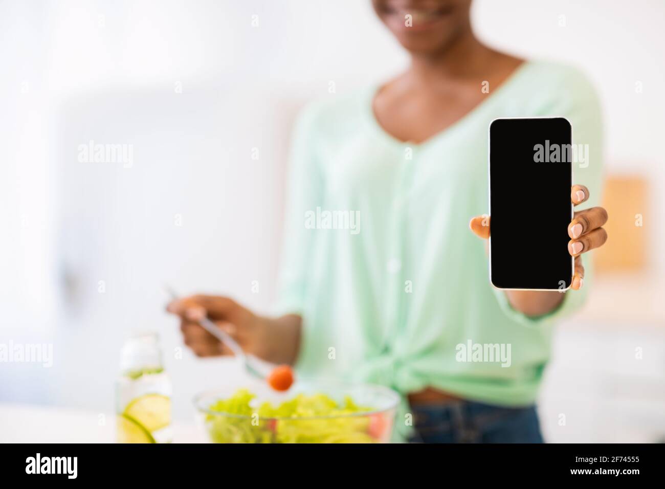 Unriconoscable African Female che mostra schermo del telefono cottura in cucina, ritagliato Foto Stock