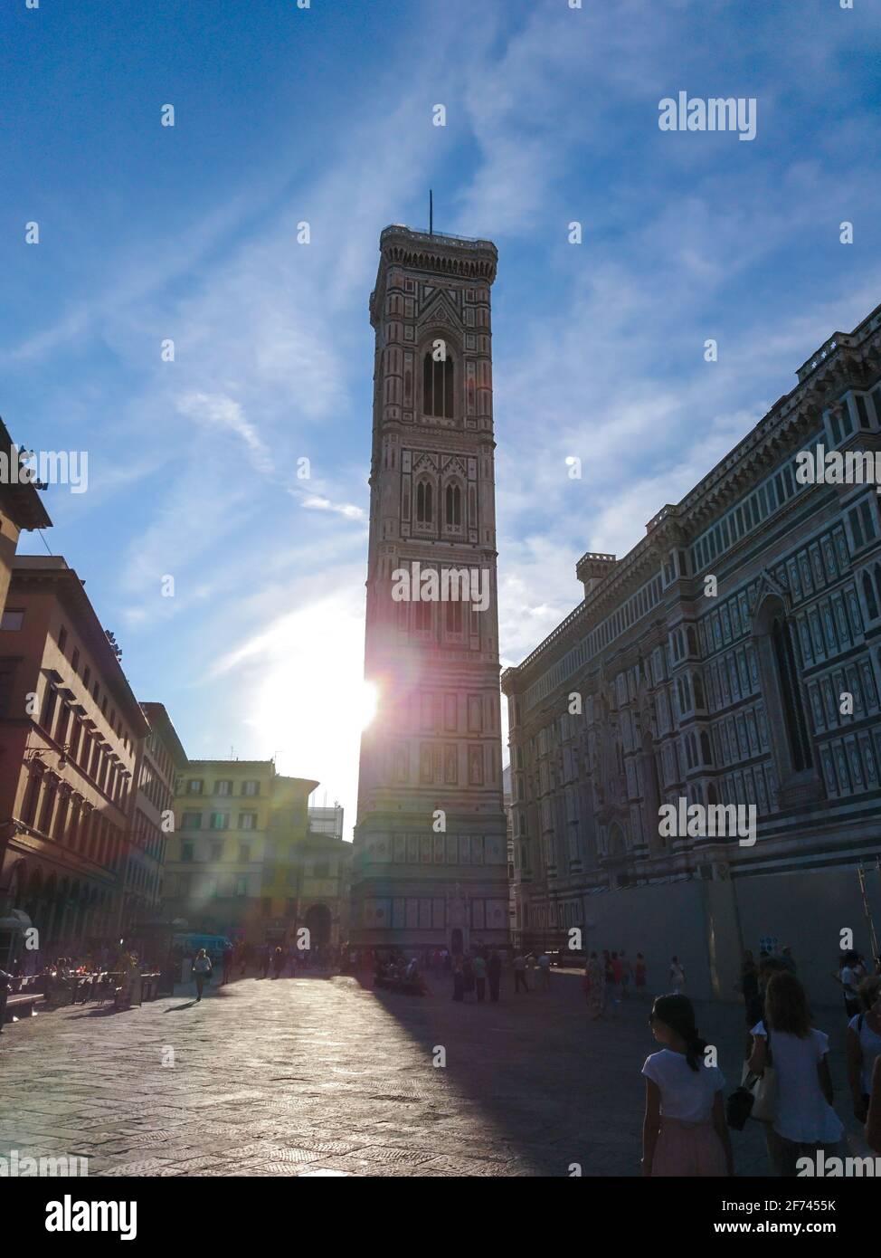 Firenze, Italia - 12 agosto 2019: Il campanile di Giotto e la Cattedrale di Santa Maria del Fiore si affacciano sulla strada con il sole luminoso. Facciata in marmo colorato con bl Foto Stock