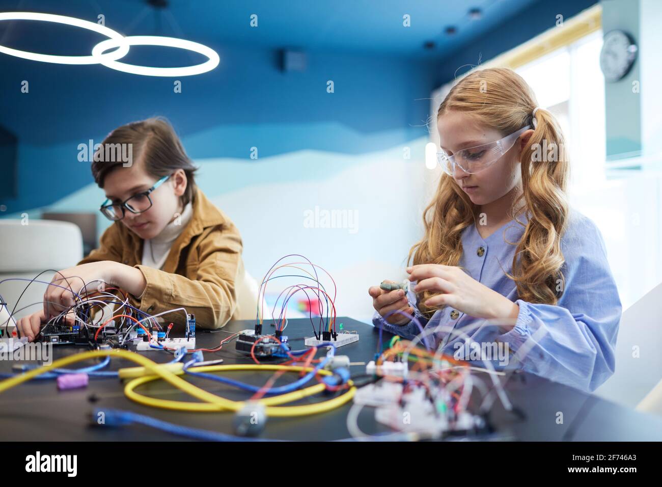 Ritratto di due bambini che costruiscono robot e sperimentano con l'elettricità circuiti in classe ingegneristica a scuola Foto Stock