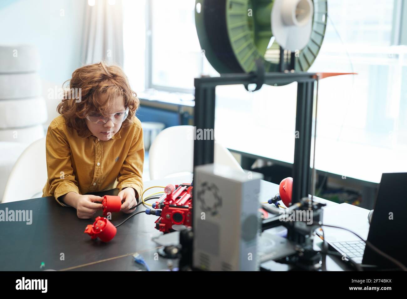 Ritratto di carino capelli ricci ragazzo costruzione barca robot durante la classe di ingegneria a scuola moderna, copia spazio Foto Stock