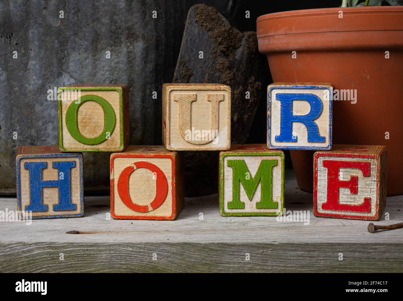 'La nostra casa' scritto in blocchi di legno d'epoca con sfondo giardinaggio. Foto Stock