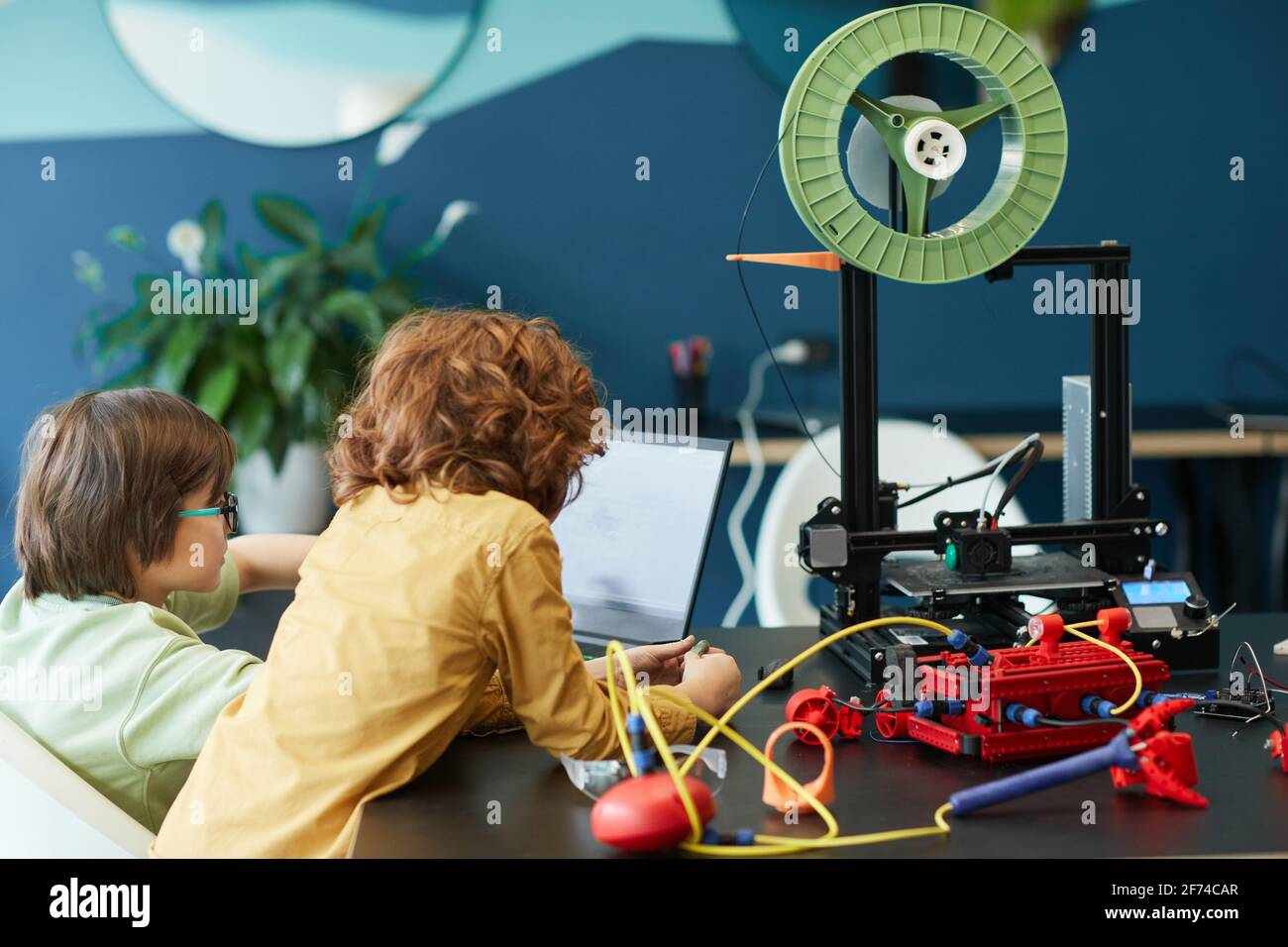 Vista posteriore a due ragazzi che costruiscono robot e che utilizzano una stampante 3D durante la lezione di ingegneria a scuola, copia spazio Foto Stock