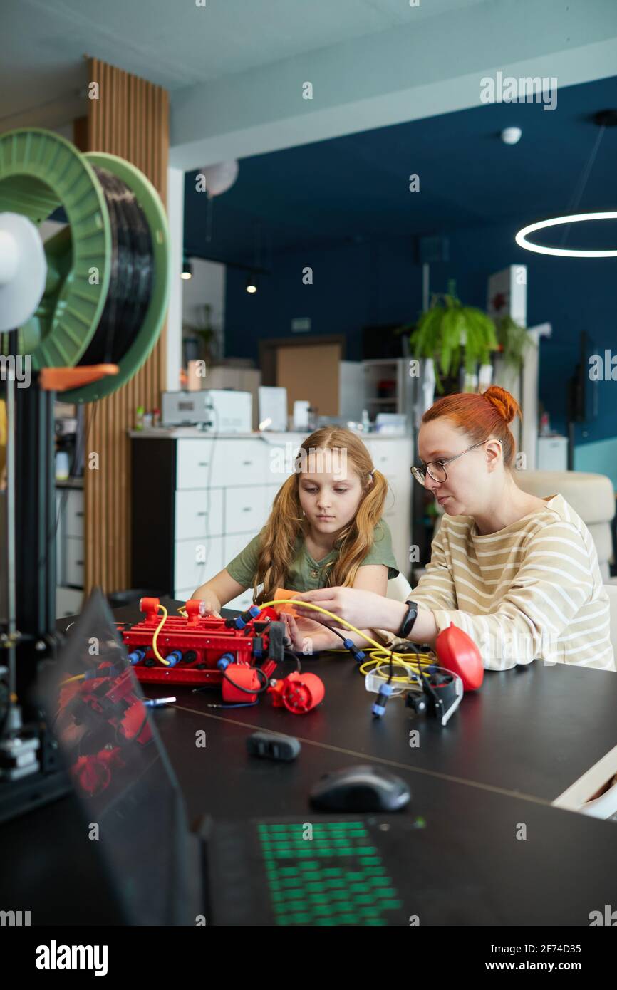 Ritratto verticale della giovane insegnante che aiuta la ragazza a costruire robot durante la lezione di ingegneria alla scuola moderna Foto Stock