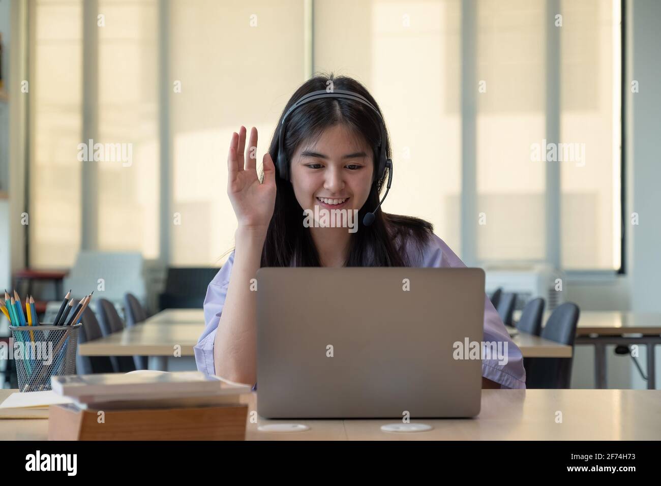 Sorridente ragazza asiatica in cuffie hanno videochiamata classe distante con insegnante utilizzando il laptop, felice bambino onda saluto con tutor, studio on-line su Foto Stock