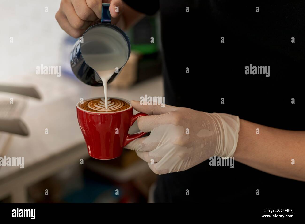 Primo piano barista che versa il latte in cottura a vapore nella tazza da  caffè, creando