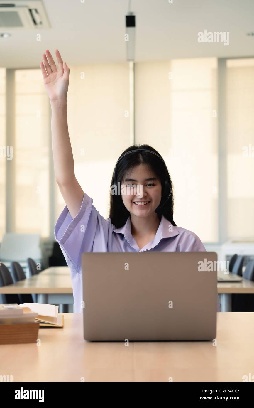 Sorridente ragazza asiatica in cuffie hanno videochiamata classe distante con insegnante utilizzando il laptop, felice bambino onda saluto con tutor, studio on-line su Foto Stock