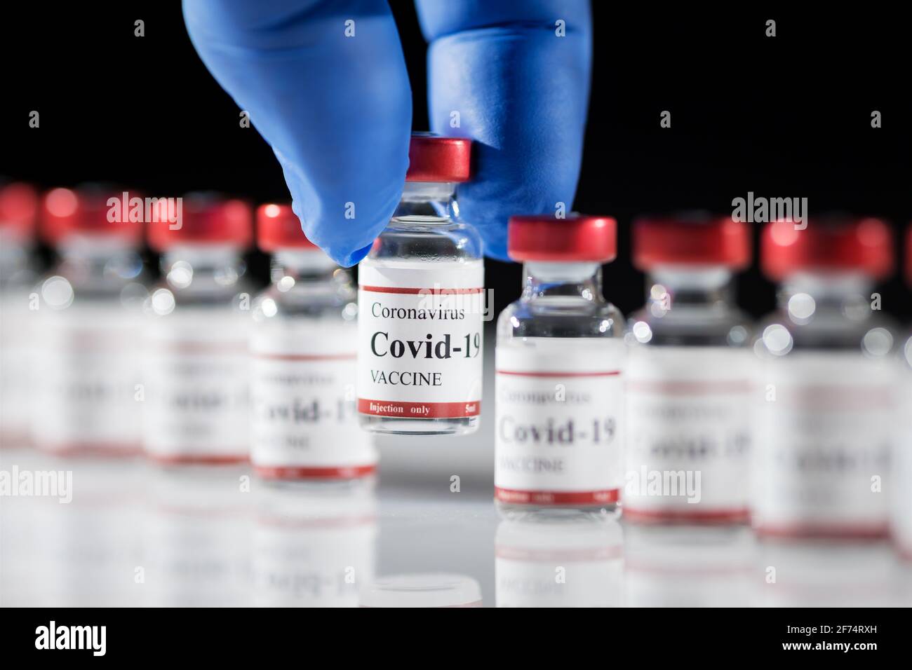 I guanti blu in lattice per i medici contengono il flaconcino di vaccino per coronavirus Covid-19. Foto Stock
