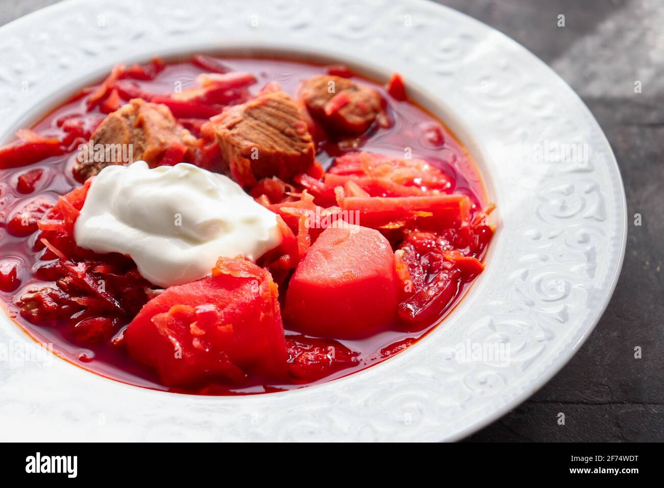 Borsch rosso con verdure e carne in un piatto bianco. Zuppa di pomodoro. Sfondo scuro. Delizioso pranzo sano. Primo piano Foto Stock
