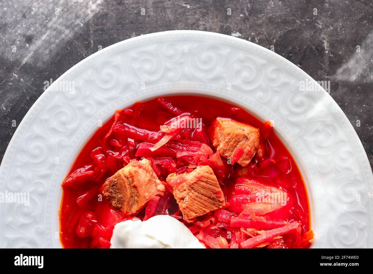Borsch rosso con verdure e carne in un piatto bianco. Zuppa di pomodoro. Sfondo scuro. Delizioso pranzo sano. Primo piano Foto Stock