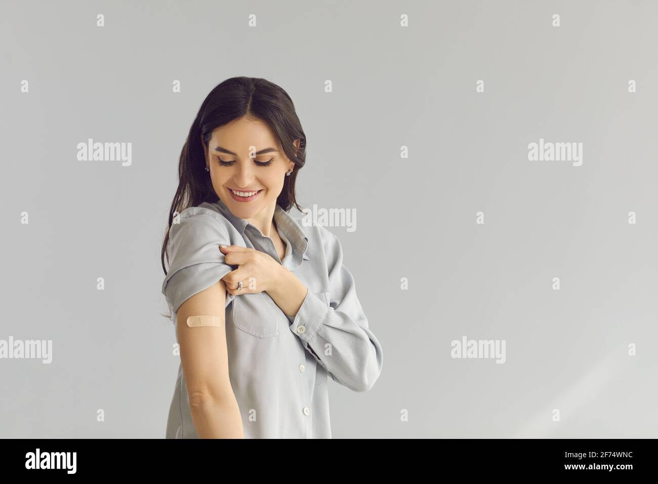 Felice giovane signora su copy space sfondo sorridente e mostrando braccio dopo l'iniezione del vaccino Foto Stock