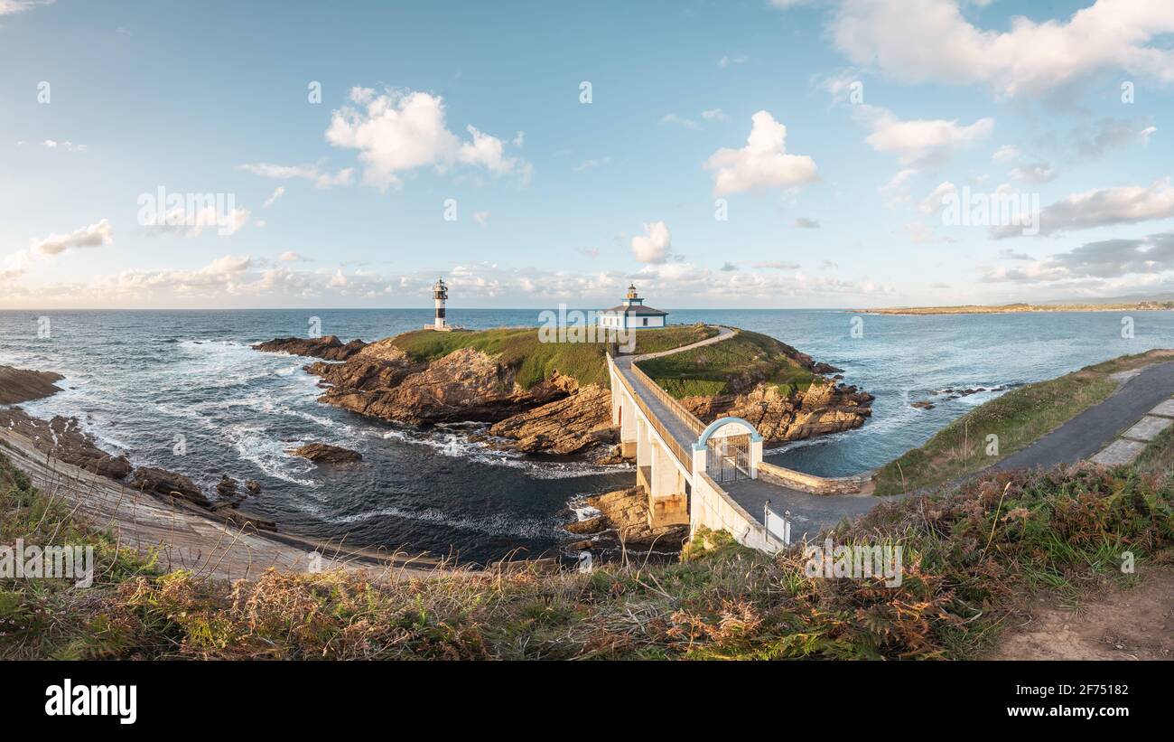Spettacolare scenario di ponte che conduce a un'isola rocciosa coperta da Erba verde con faro posto in oceano ondulato a Faro Illa Pancha in Galizia in Foto Stock