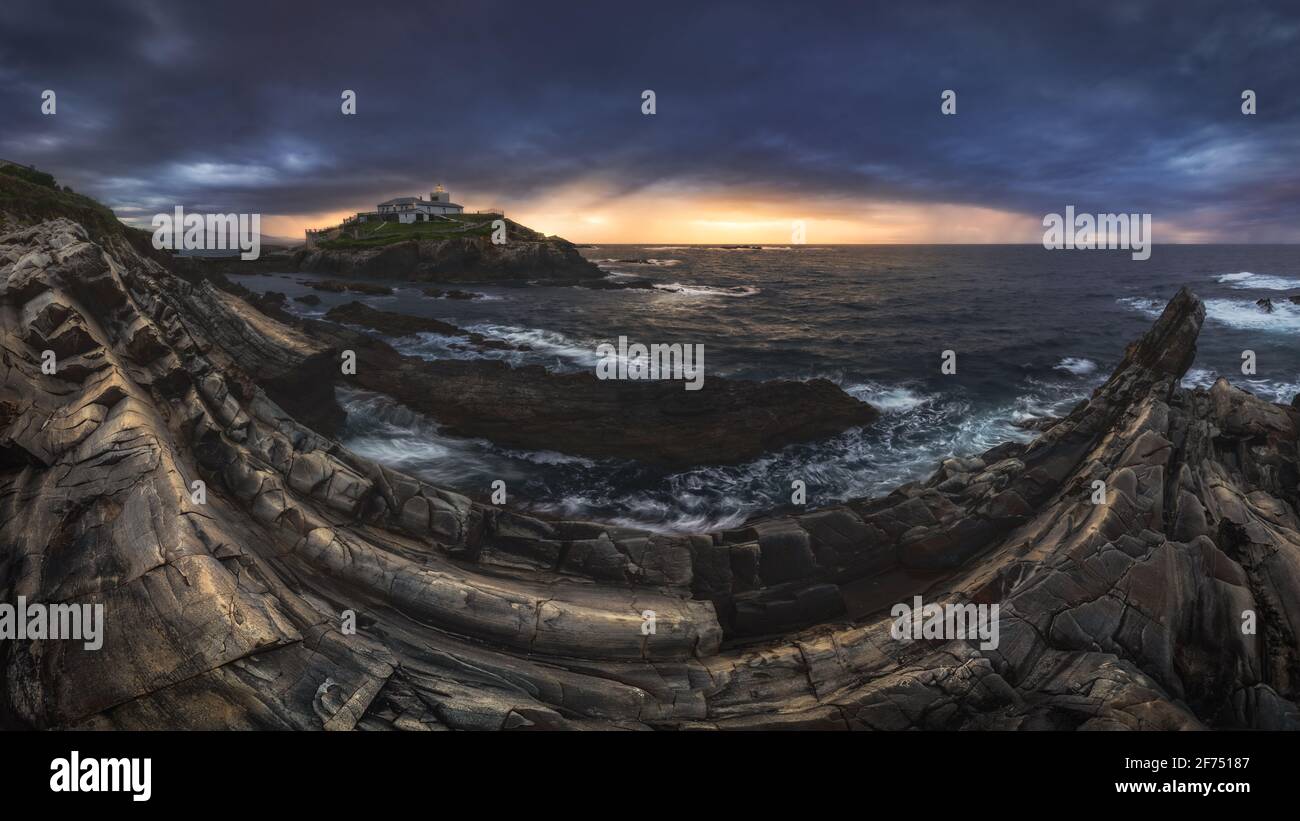 Scenario mozzafiato di isola rocciosa con faro situato in oceano Vicino costa rocciosa a Faro Tapia de Casariego nelle Asturie In Spagna sotto la nuvolosa sk Foto Stock