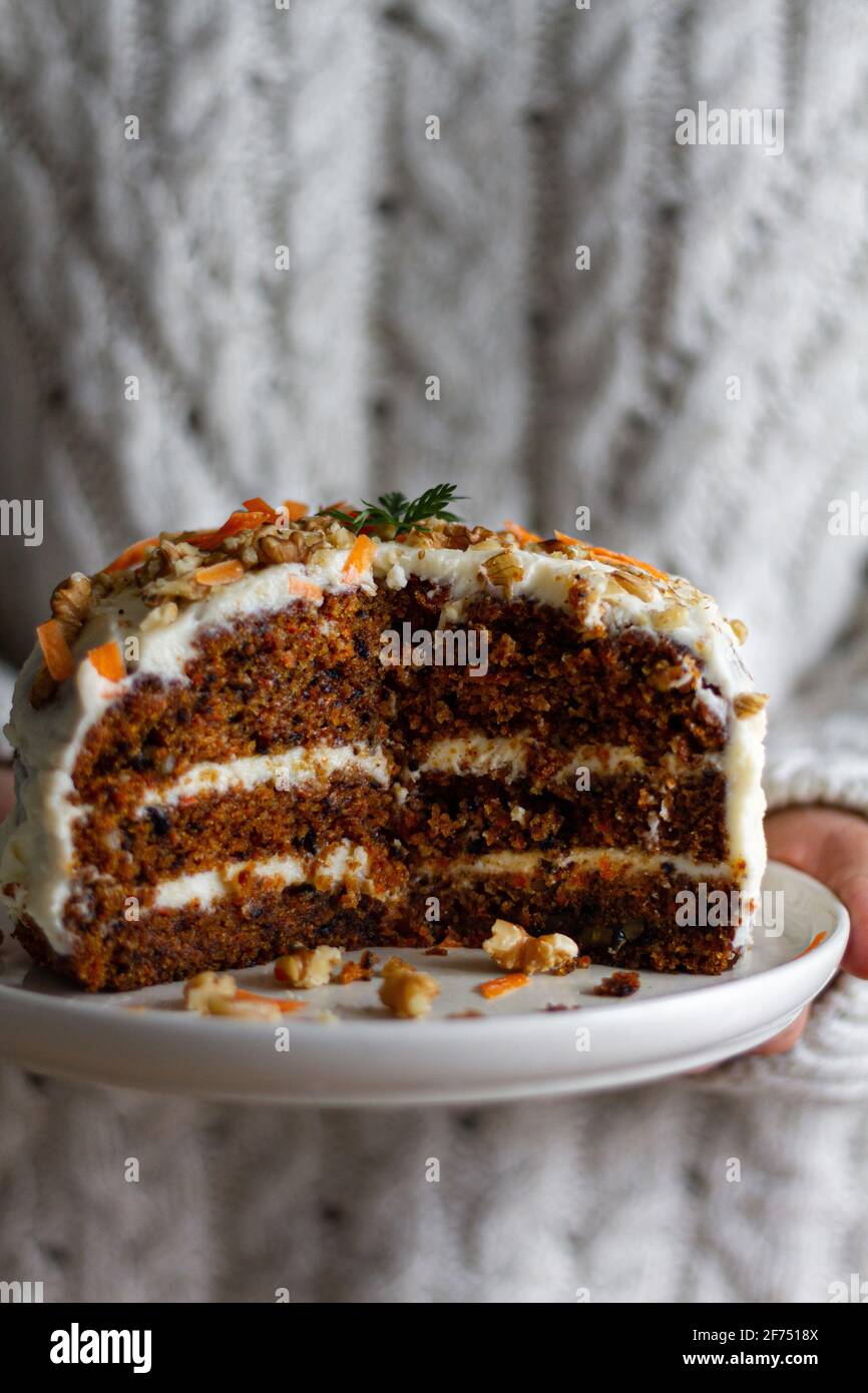 Crop anonimo piatto di tenuta cuoco con torta gustosa con crema formaggio e biscotto umido decorato con noci tritate e carote sezioni Foto Stock