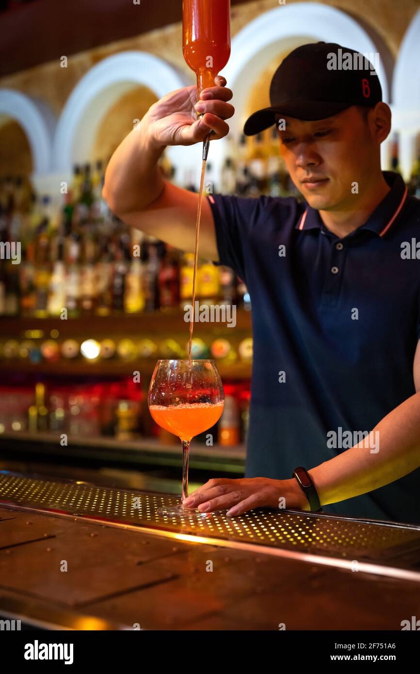 Giovane barista asiatico che versa succo di pompelmo nel bicchiere preparazione di un cocktail al bar Foto Stock