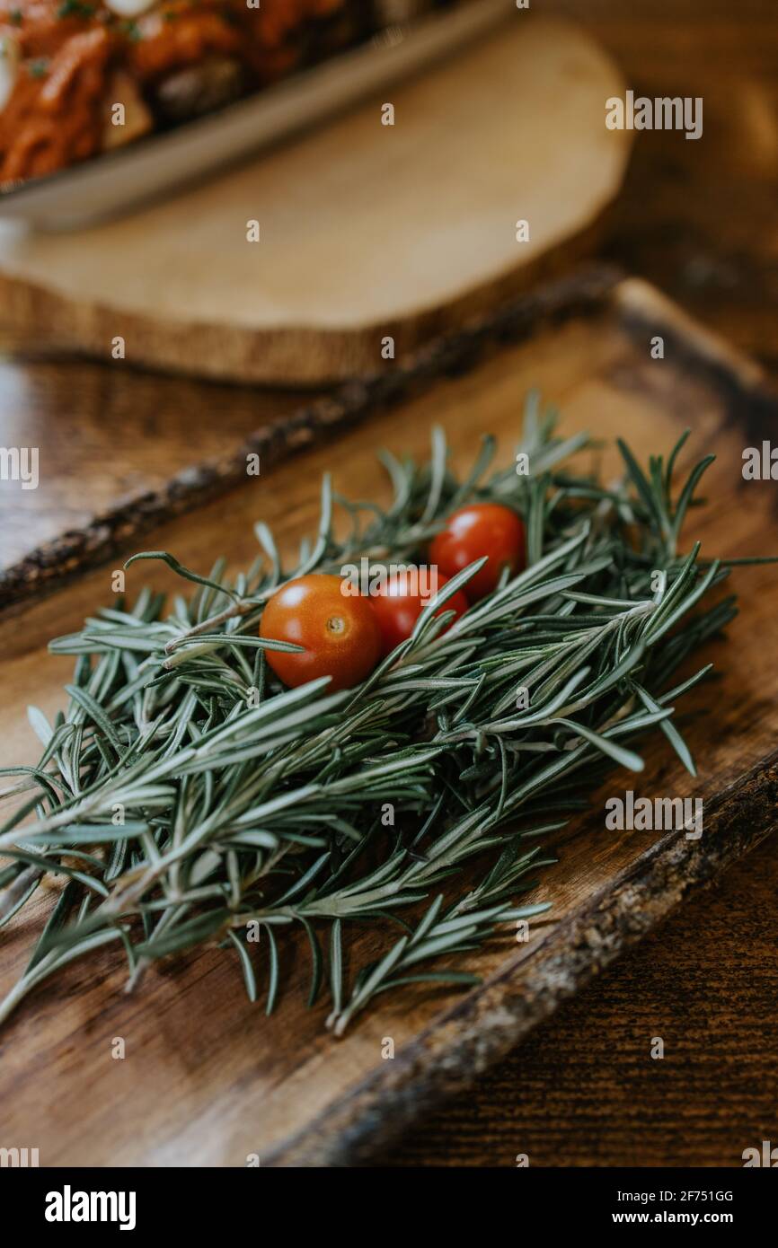 Dall'alto di pomodori ciliegini maturi interi su rosmarino fresco ciuffi con piacevole profumo su piastra di legno Foto Stock