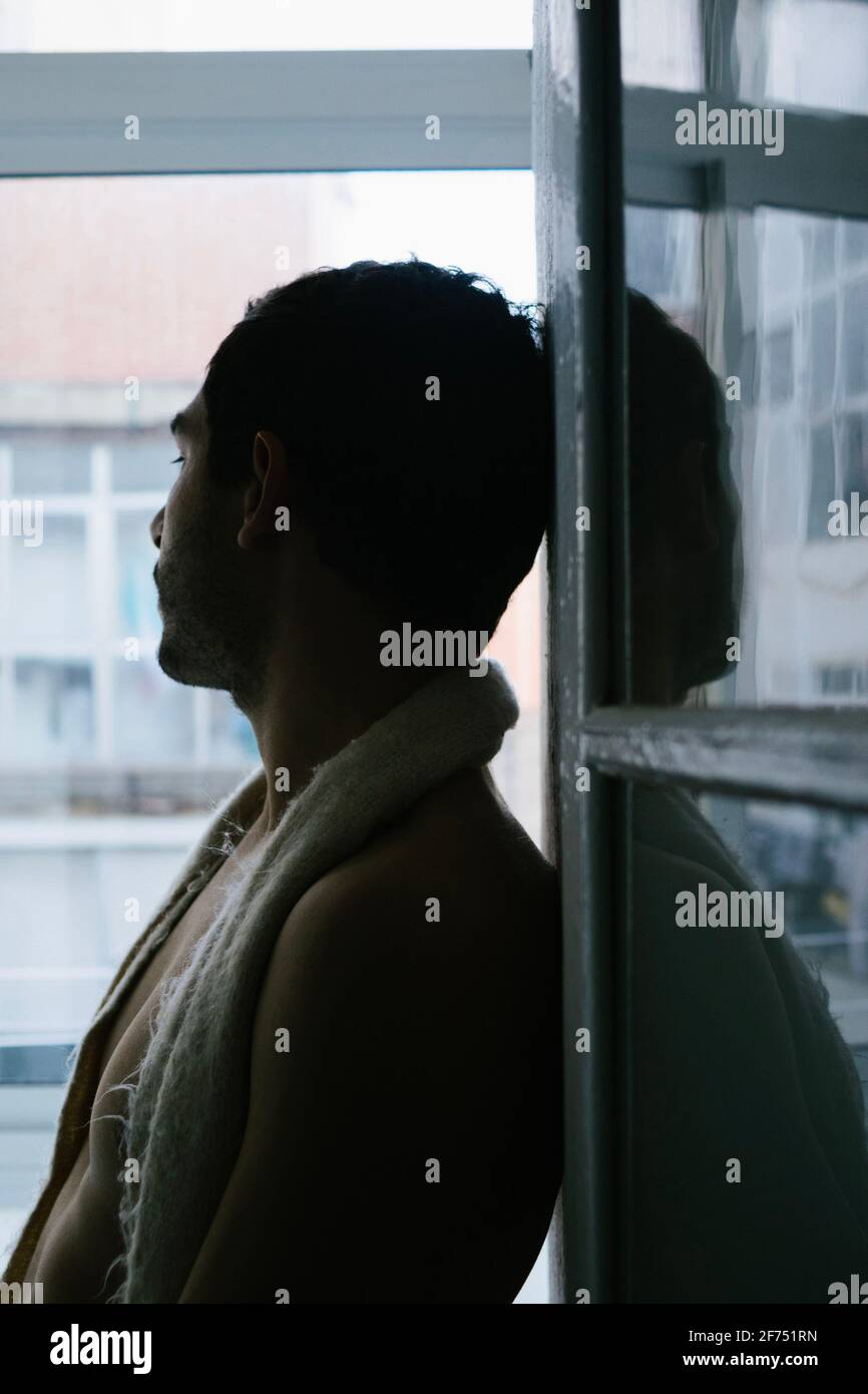 Vista laterale del maschio pensivo seduto sul davanzale a casa Foto Stock