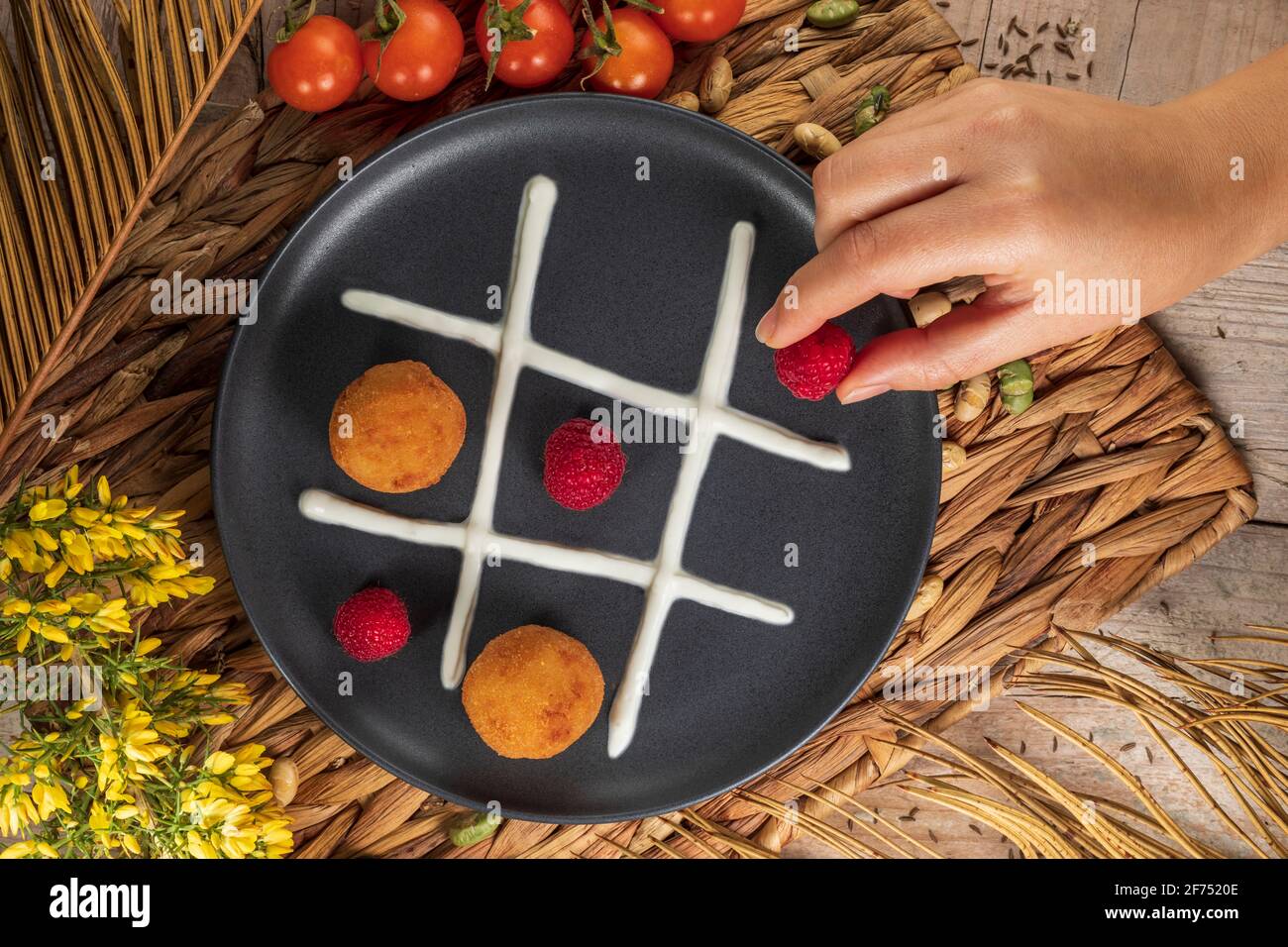 Vista dall'alto del prodotto cuoco irriconoscibile che mette il lampone intero sopra piatto con frittelle e panna montata che rappresenta noughts e croci gioco Foto Stock