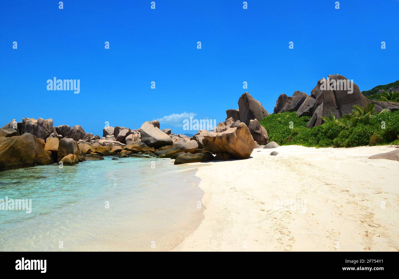 Spiaggia di Anse Marron con grandi massi di granito sull'isola di la Digue, Seychelles. Paesaggio tropicale con cielo soleggiato. Destinazione di viaggio di lusso. Foto Stock