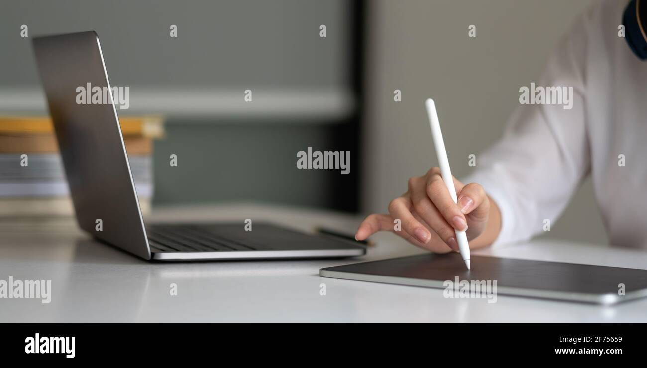 Primo piano mano di donna con penna stilo scrittura su blocco note digitale,  toccando lo schermo del tablet digitale che lavora sul computer portatile  in ufficio. Web Foto stock - Alamy