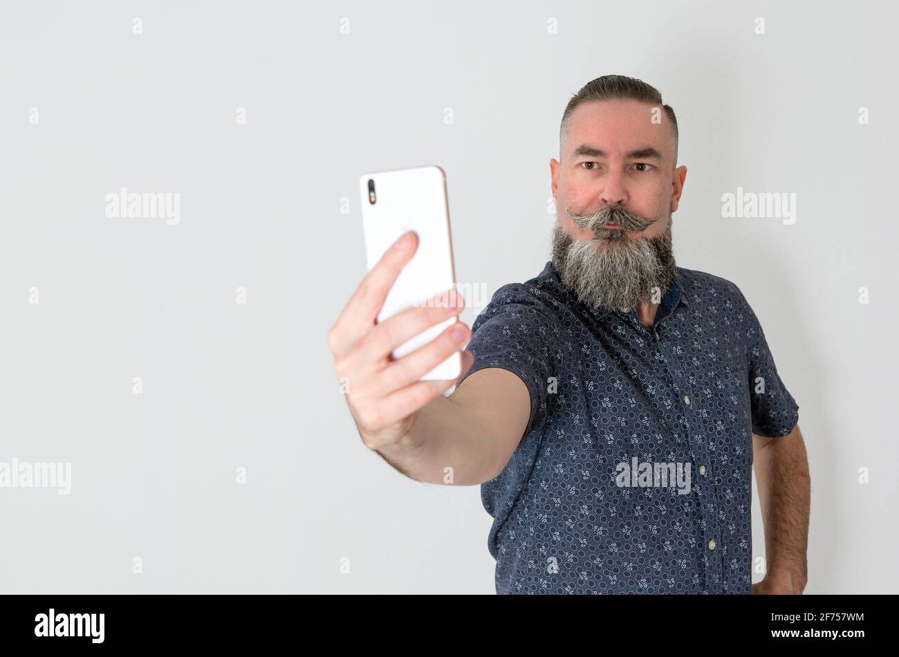 Stile hipster bearded con aspetto caucasico 40-45 anni utilizzando lo smartphone per prendere un ritratto di auto, selfie. Fuoco selettivo Foto Stock