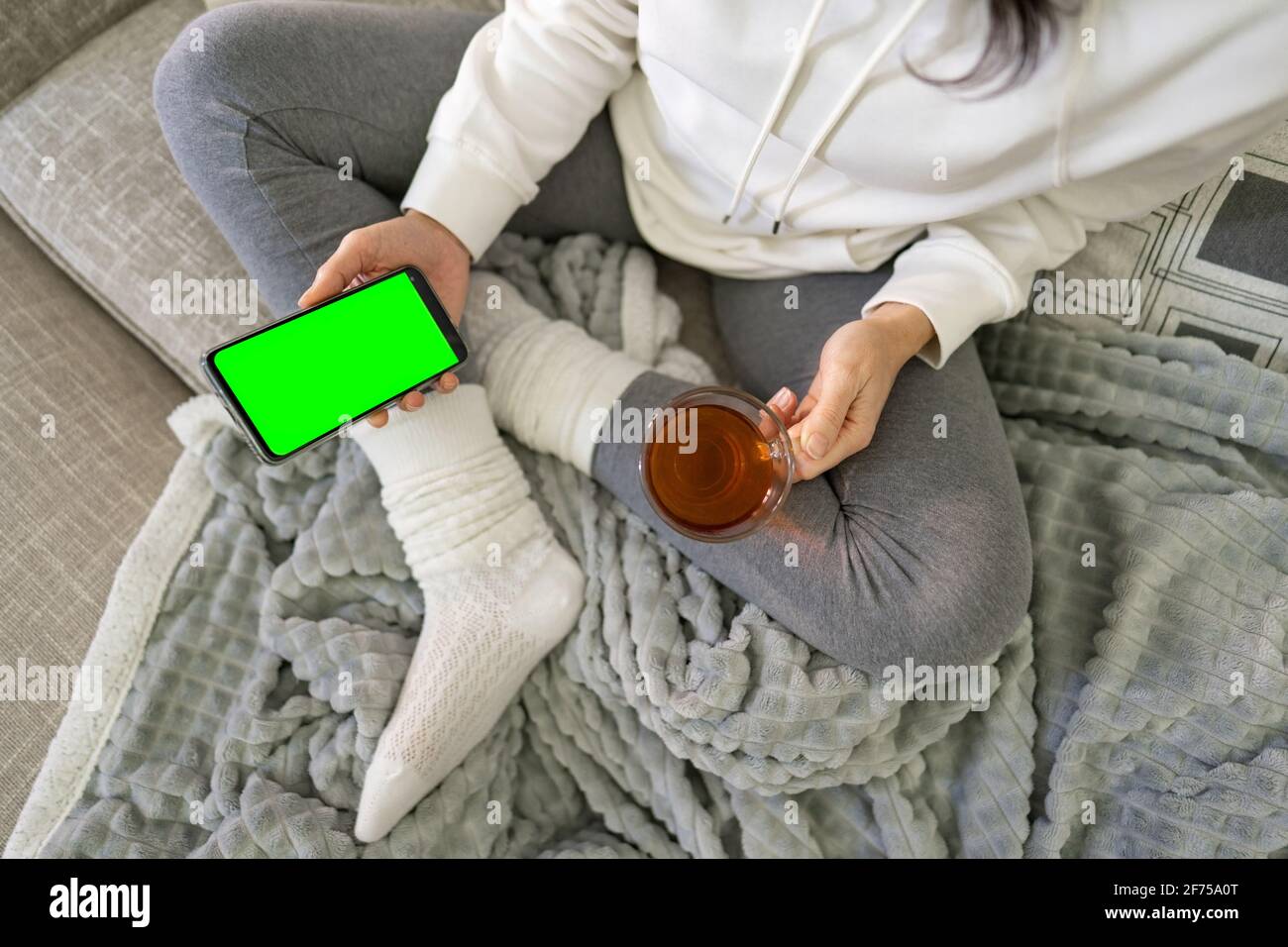I giovani trascorrono del tempo a casa utilizzando lo smartphone per chattare in una rete semplice. Vista dalla parte superiore della giovane donna annoiata che tiene la cella con schermo verde dispensa Foto Stock