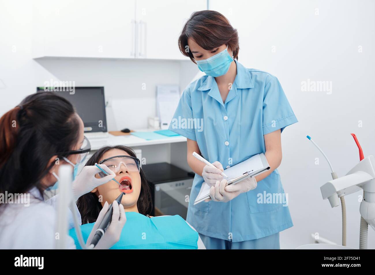 Dentista che esamina i denti della paziente femminile quando l'infermiere prende appunti nel documento Foto Stock