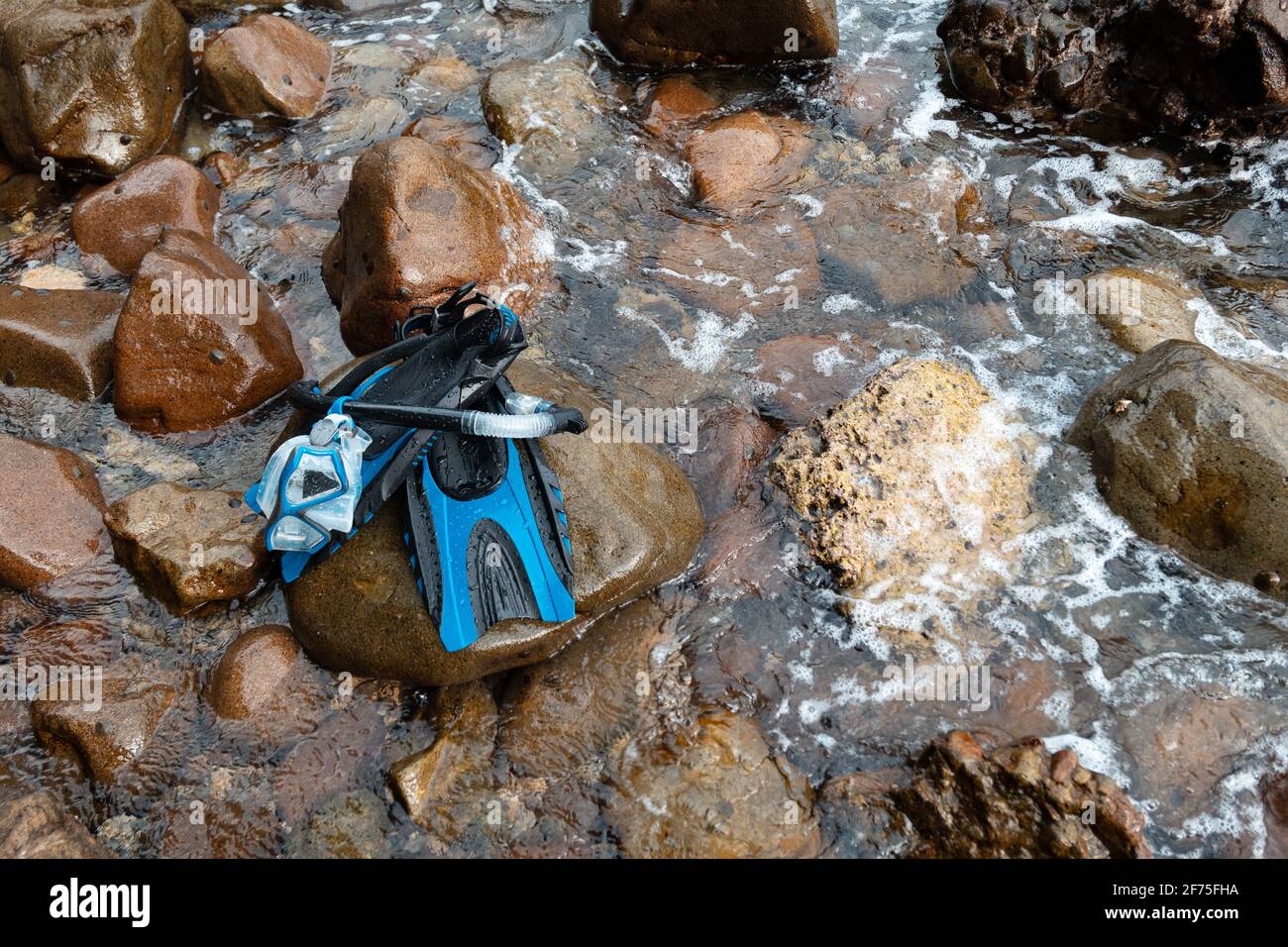 Una serie di maschera blu, snorkeling e pinne riposano sulle rocce vicino alla riva dell'isola durante una vacanza Foto Stock