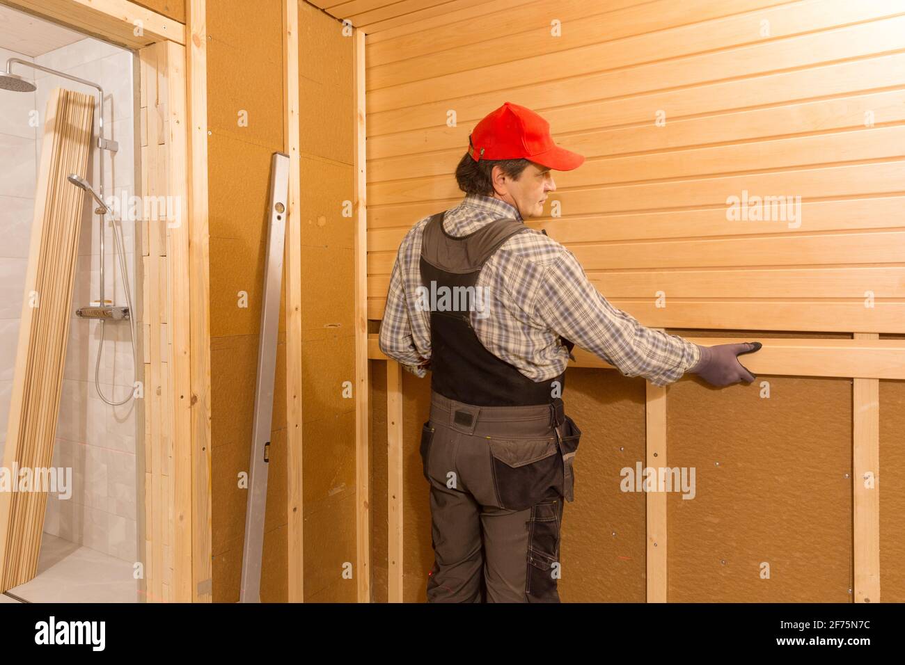 Costruzione di sauna, rifinitura. L'uomo sta avvitando una panca di legno al muro. Foto Stock