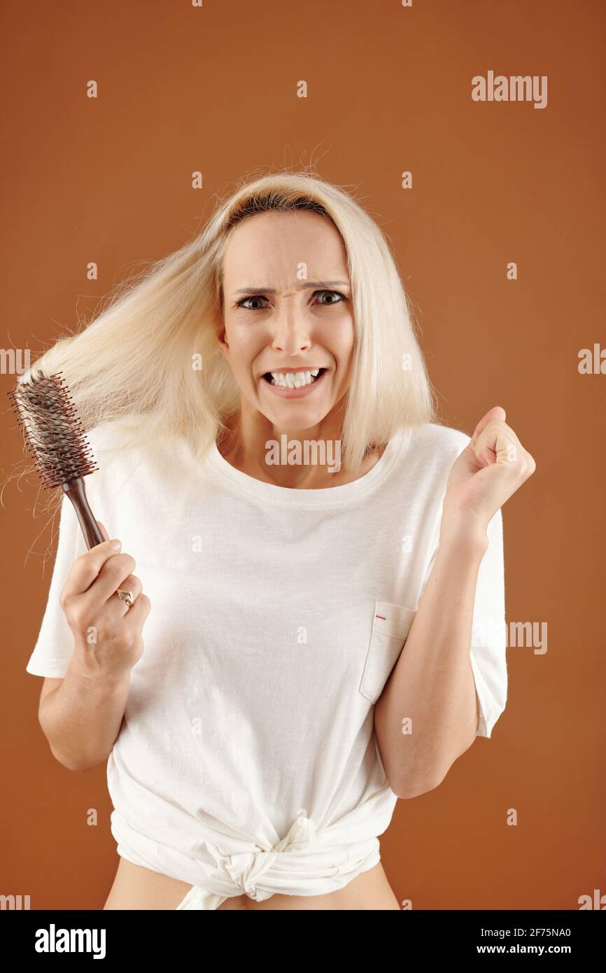 La giovane donna irritata non può spazzolare la sua bionda secca aggrovigliata capelli Foto Stock