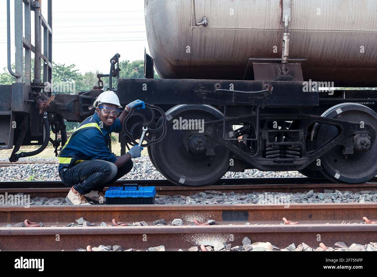 Un tecnico africano che indossa casco, boschetti e giubbotto di sicurezza utilizza una chiave per riparare il treno Foto Stock
