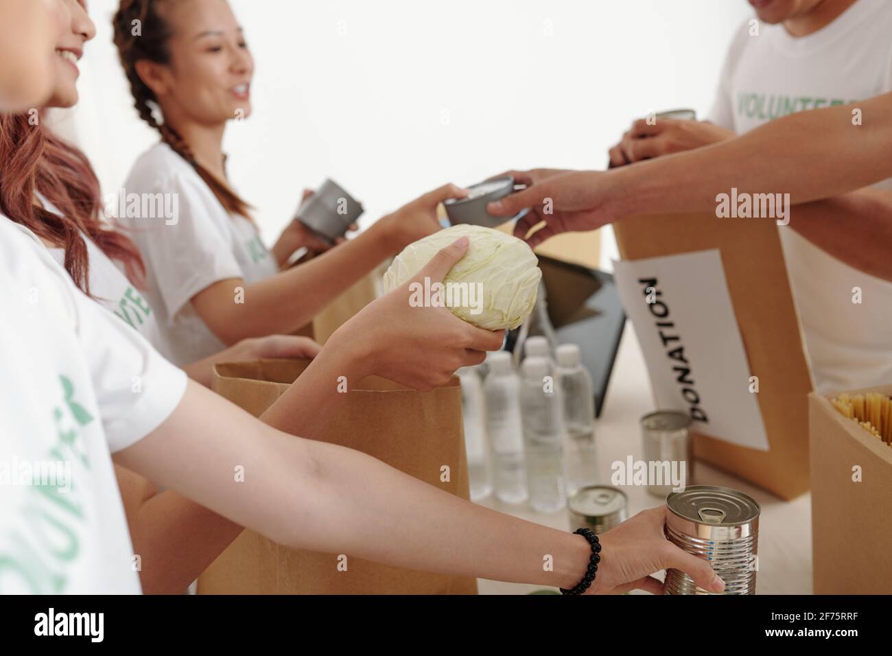 Immagine ritagliata di volontari che impacchettano acqua, cibo in scatola e verdure in confezioni di carta per le persone che hanno perso le case dopo l'uragano o alluvione Foto Stock