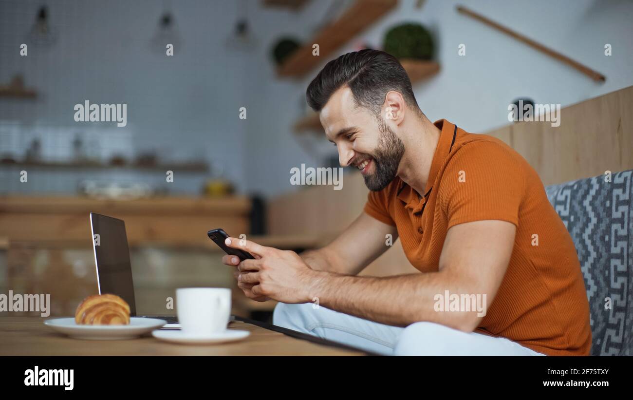 messaggi gratuiti felici sullo smartphone vicino al computer portatile e colazione in caffè Foto Stock