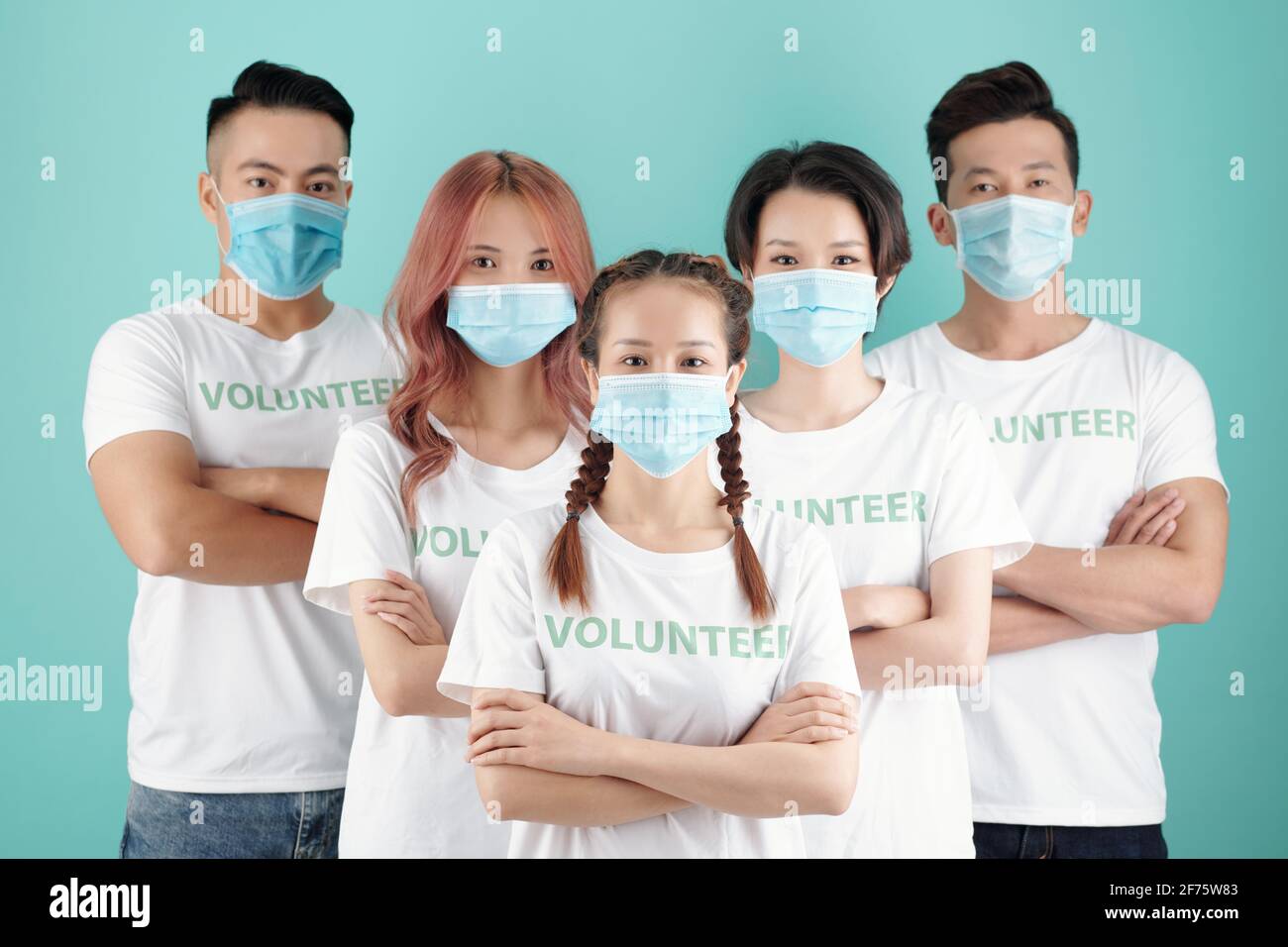 Team di giovani volontari vietnamiti in maschere protettive in piedi dietro il loro leader femminile Foto Stock