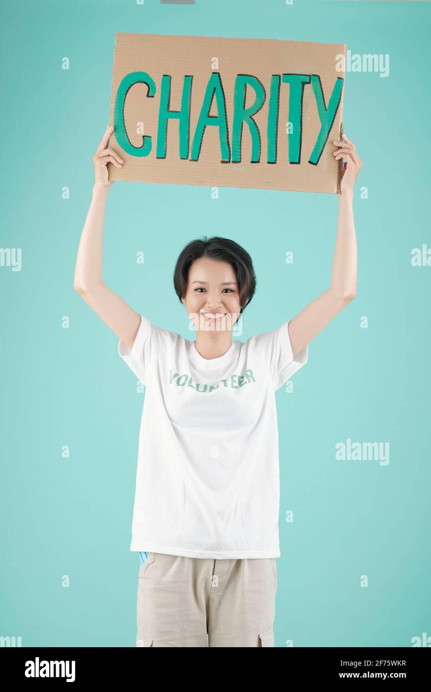 Sorridente giovane volontario asiatico in piedi con un cartello di beneficenza, isolato su azzurro Foto Stock