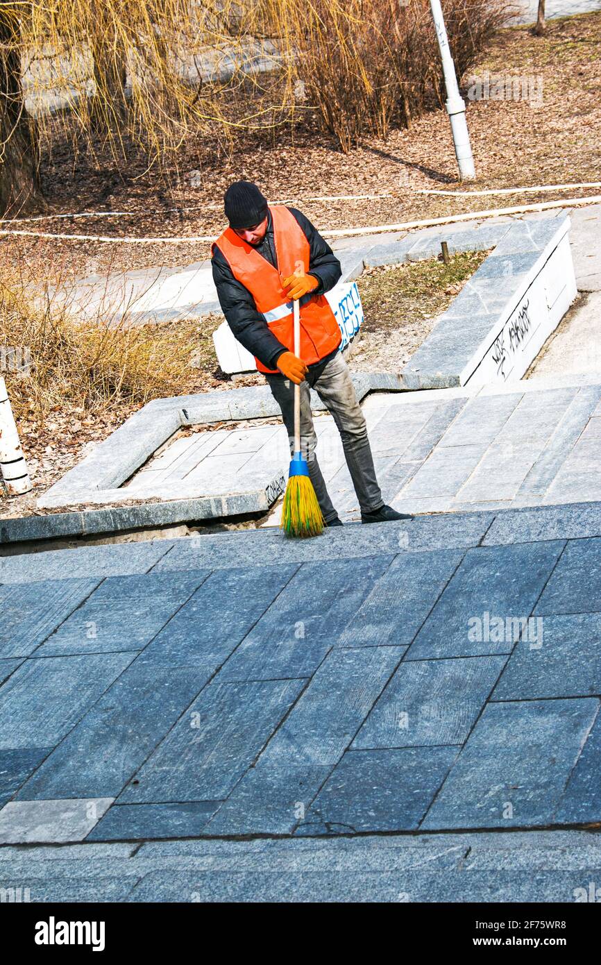 Dnepropetrovsk, Ucraina - 03.16.2021: I servizi municipali stanno pulendo la città dopo l'inverno. Un lavoratore spazza una scala di granito in un parco da ultimo y Foto Stock