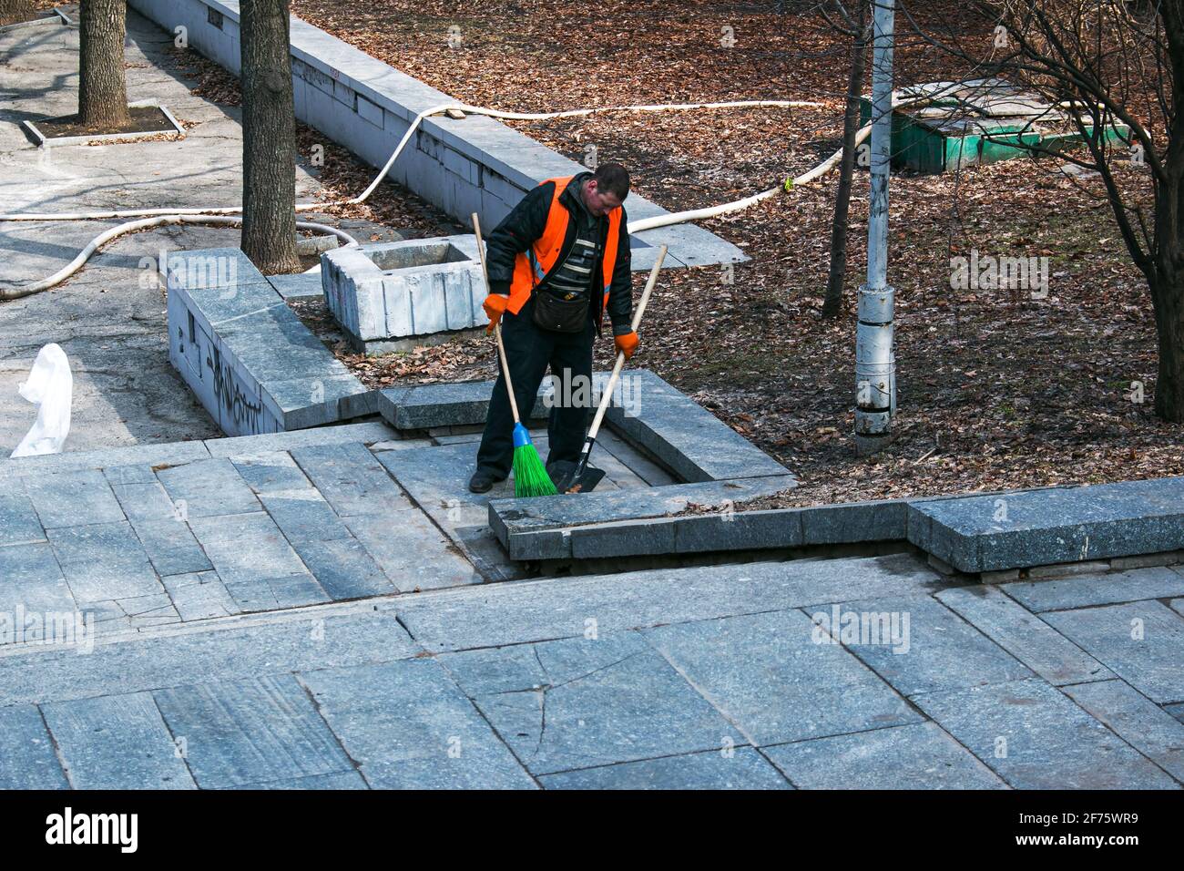 Dnepropetrovsk, Ucraina - 03.16.2021: I servizi municipali stanno pulendo la città dopo l'inverno. Un lavoratore spazza una scala di granito in un parco da ultimo y Foto Stock