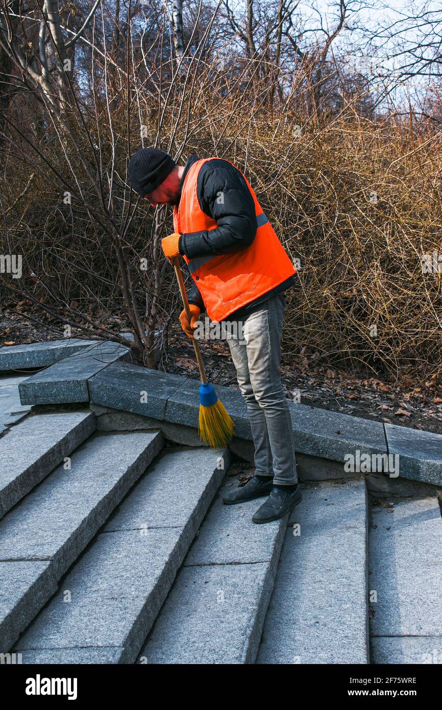 Dnepropetrovsk, Ucraina - 03.16.2021: I servizi municipali stanno pulendo la città dopo l'inverno. Un lavoratore spazza una scala di granito in un parco da ultimo y Foto Stock