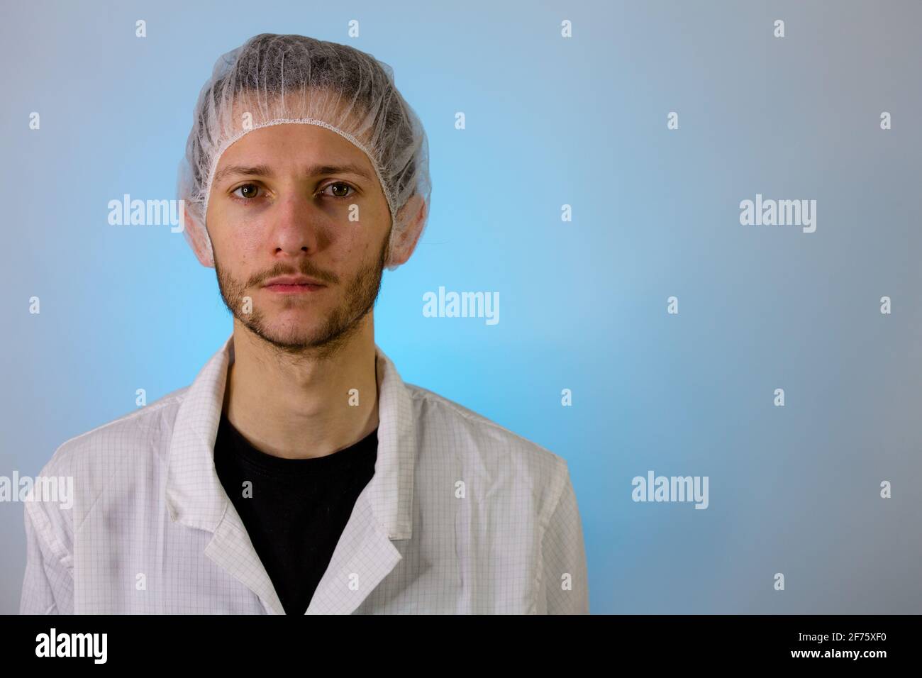 Un maschio adulto vestito in un camice bianco da laboratorio con una rete di capelli su. Pronto per lavorare in una camera bianca o in un laboratorio Foto Stock