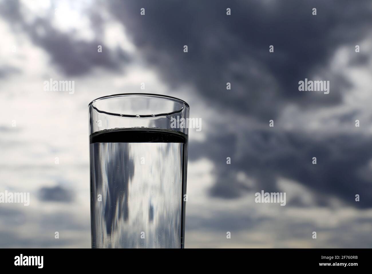 Bicchiere da bere con acqua pulita sullo sfondo del cielo scuro con le nuvole di tempesta Foto Stock