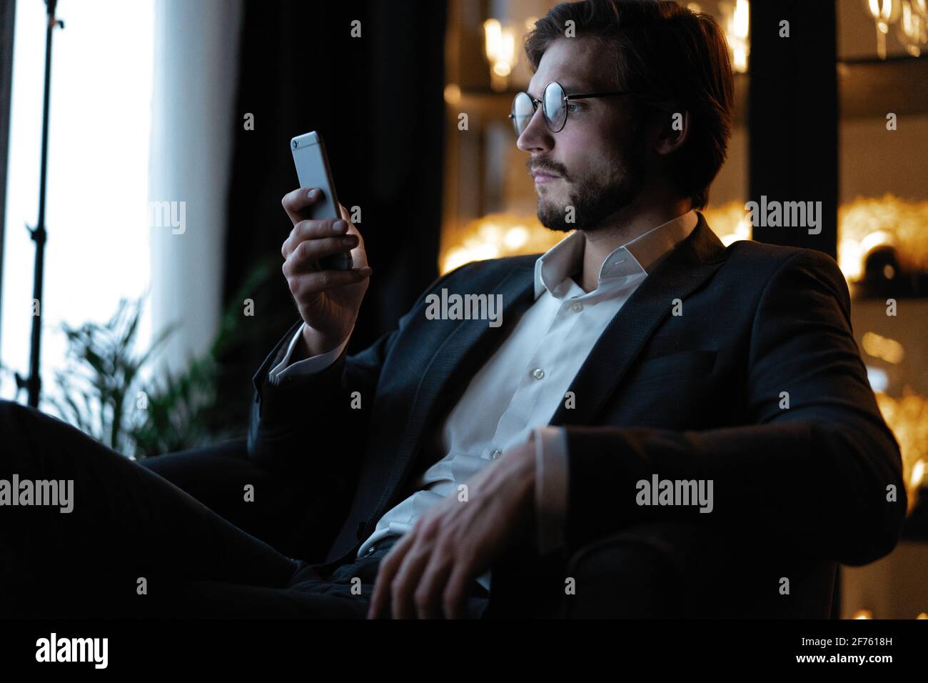 Bel giovane che usa lo smartphone durante la notte. Primo piano di messaggi di uomini d'affari sul cellulare di notte in caffetteria. Foto Stock