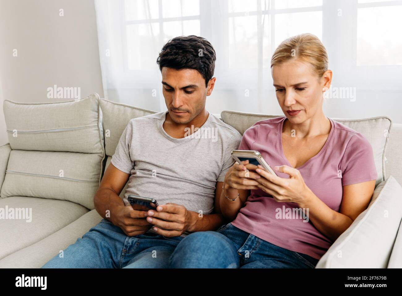 Impegnato marito e moglie caucasici assaliti nel proprio cellulare telefona mentre navighi sui social media e fai acquisti online su casa seduta sul divano Foto Stock