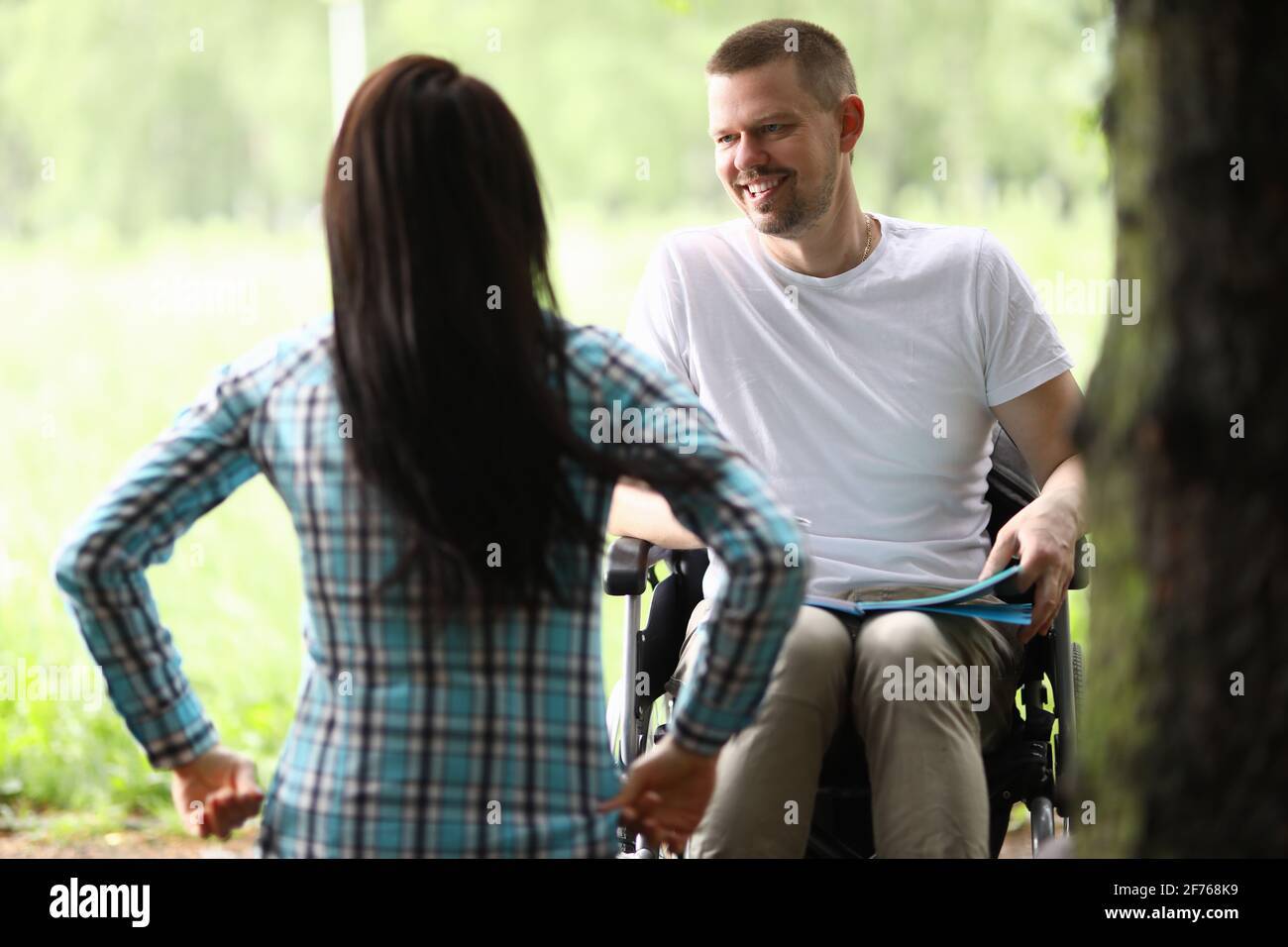 L'uomo in sedia a rotelle nel parco comunica con la donna Foto Stock