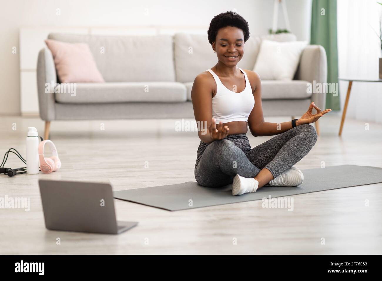 Donna afroamericana meditando al laptop facendo yoga a casa Foto Stock