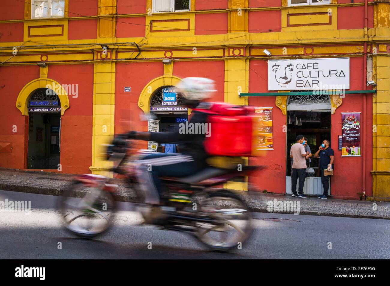 Uomini che mangiano e bevono fuori di una caffetteria. Un autista di moto per la consegna di cibo che accelera presso la caffetteria. Foto Stock