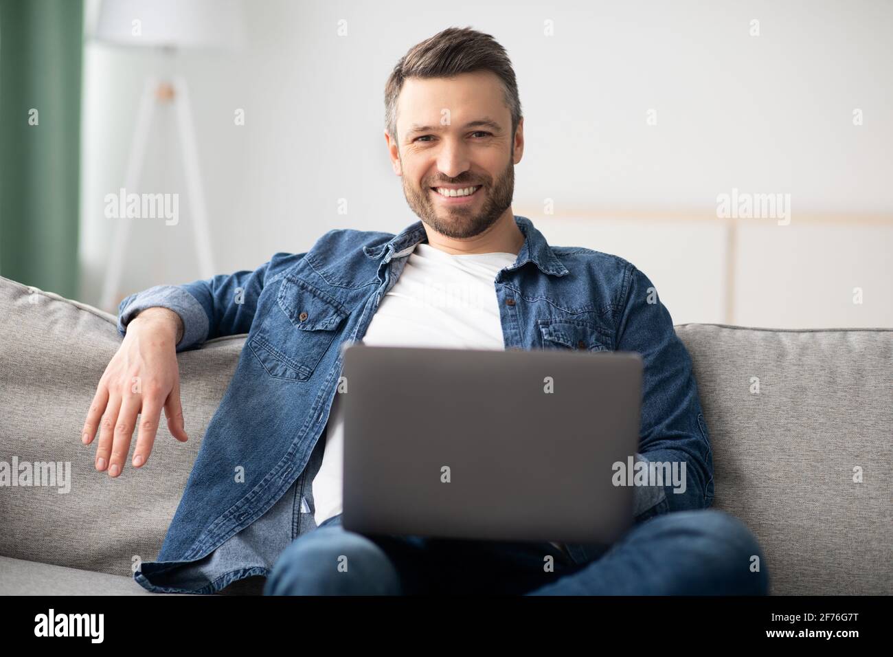 Allegro uomo di mezza età che usa il computer portatile mentre si riposa a casa Foto Stock