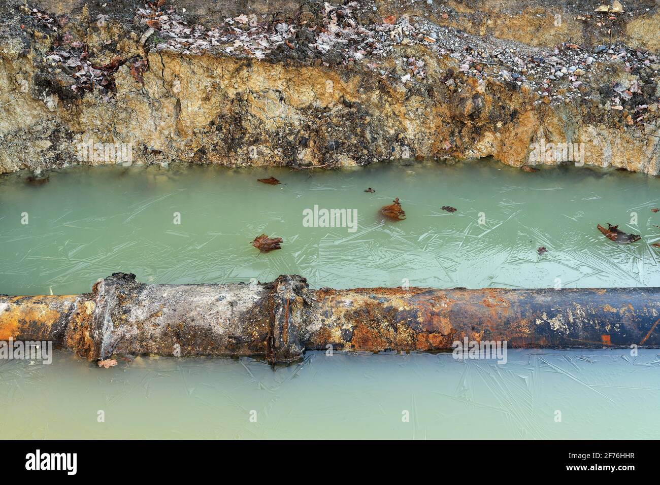 Un vecchio tubo in una fossa di costruzione. La buca piena di acque sotterranee e di acqua piovana in inverno Foto Stock