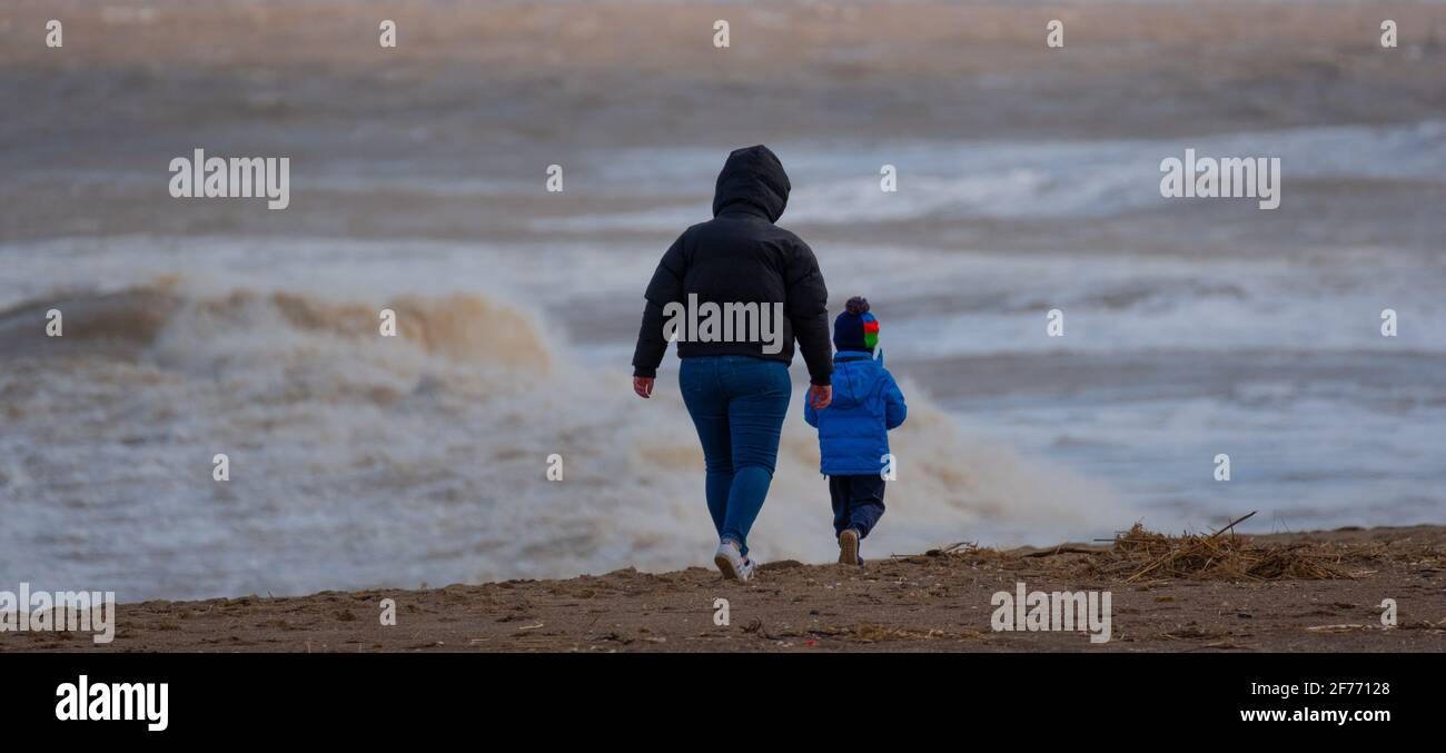 Madre e bambino fare una passeggiata sulla riva di Il Mare del Nord in una giornata fredda nel Lincolnshire Foto Stock